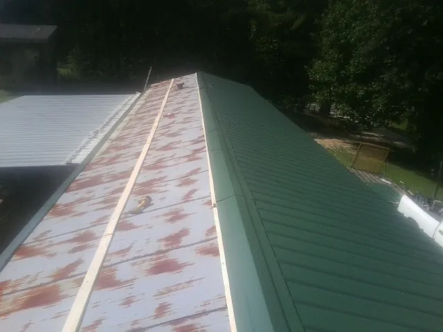Old rusted panels beside newly installed green metal roofing — Wind Damage Roof Repair by Roofing Brothers in Columbia City