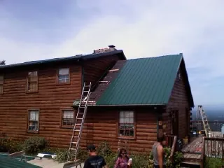 Green metal roof going on a two story log home with ladders set in Columbia City