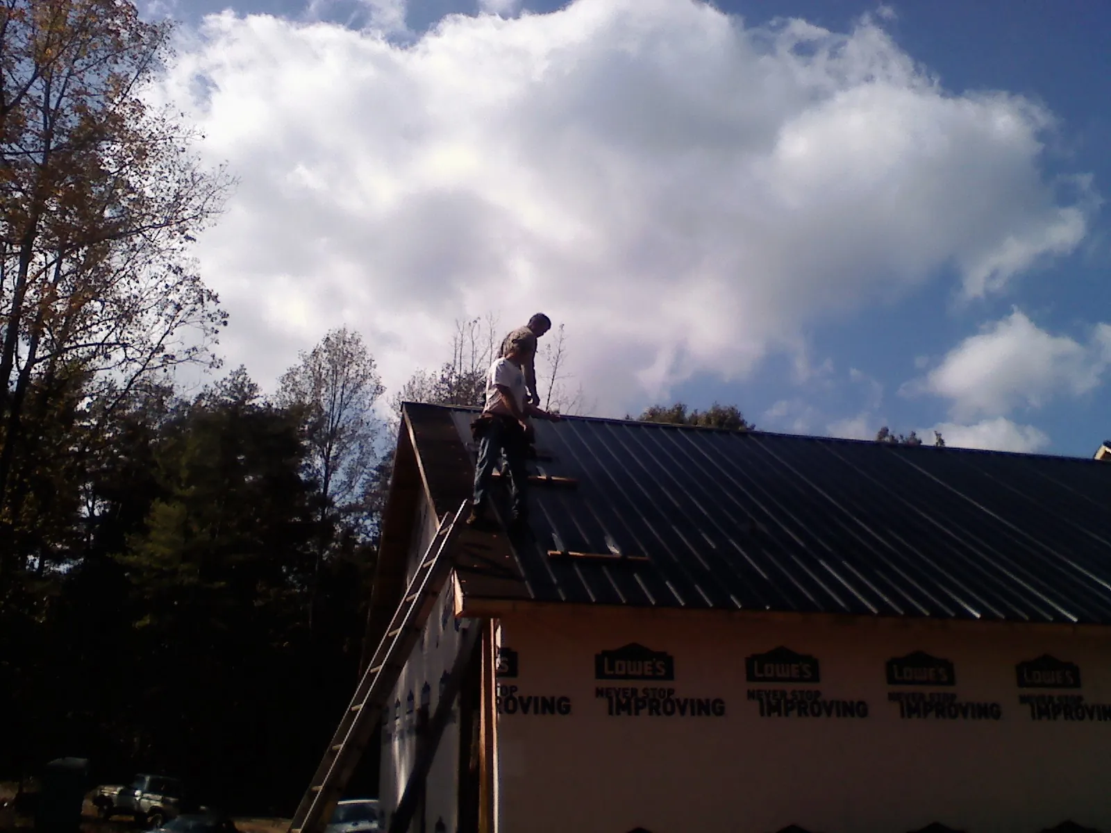 Roofer fastening dark metal panels high against a cloudy sky, from a Roof Inspection job in Columbia City
