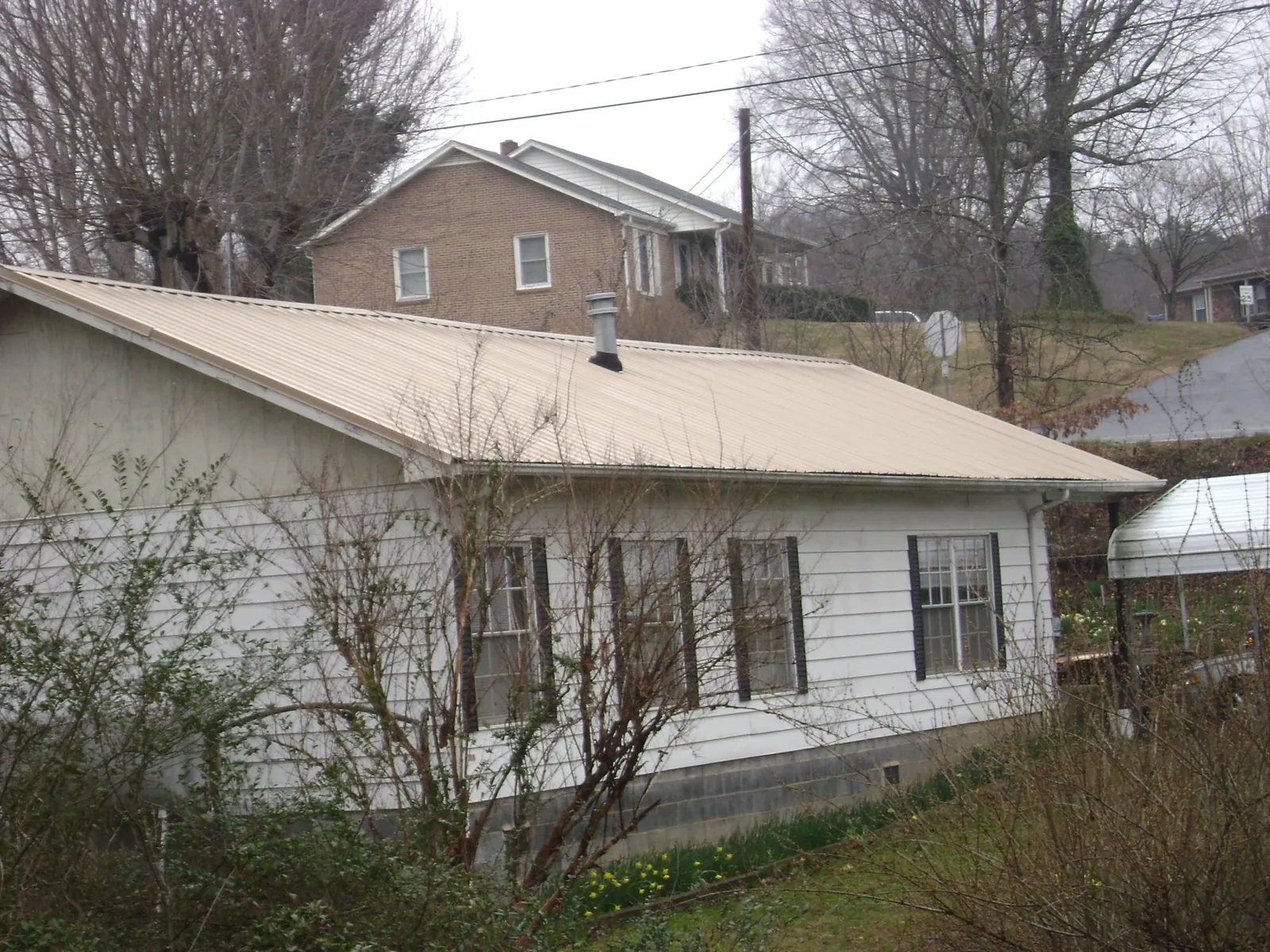 Tan metal roof on a white sided house set into a hillside — Commercial Roofing by Roofing Brothers in Columbia City